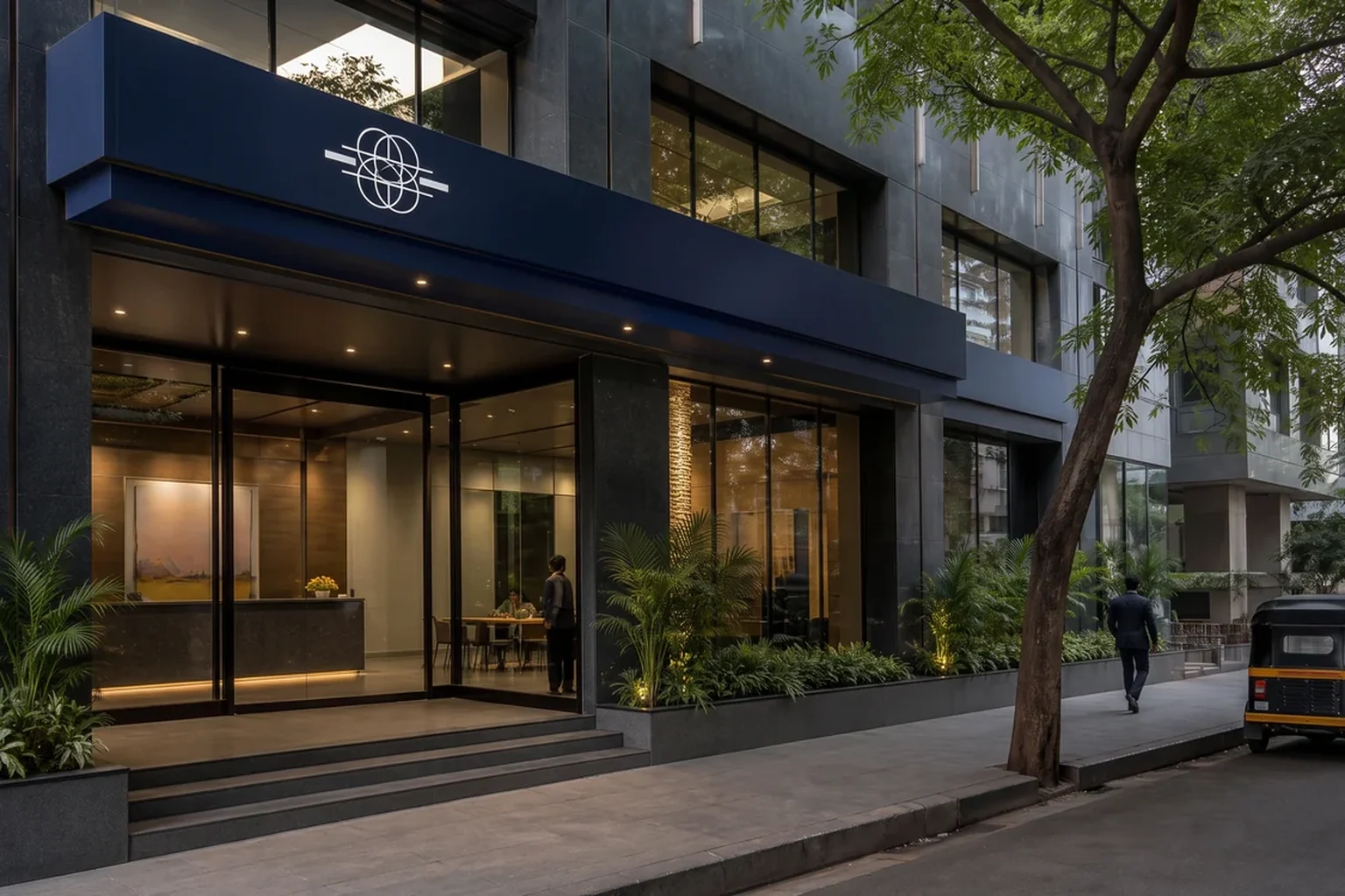 Finance branch frontage on a tree-lined street with a navy canopy fascia, an illuminated mark and a glazed entrance