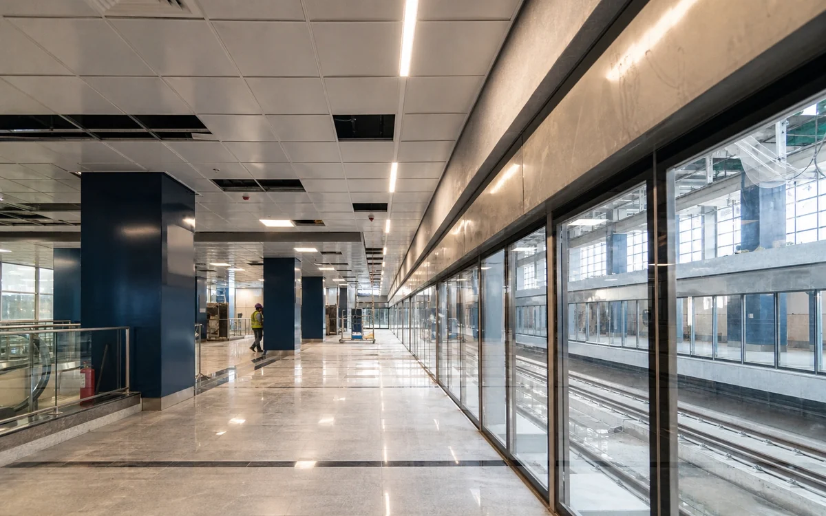 Station concourse with glazed screens along the platform edge and navy-clad columns