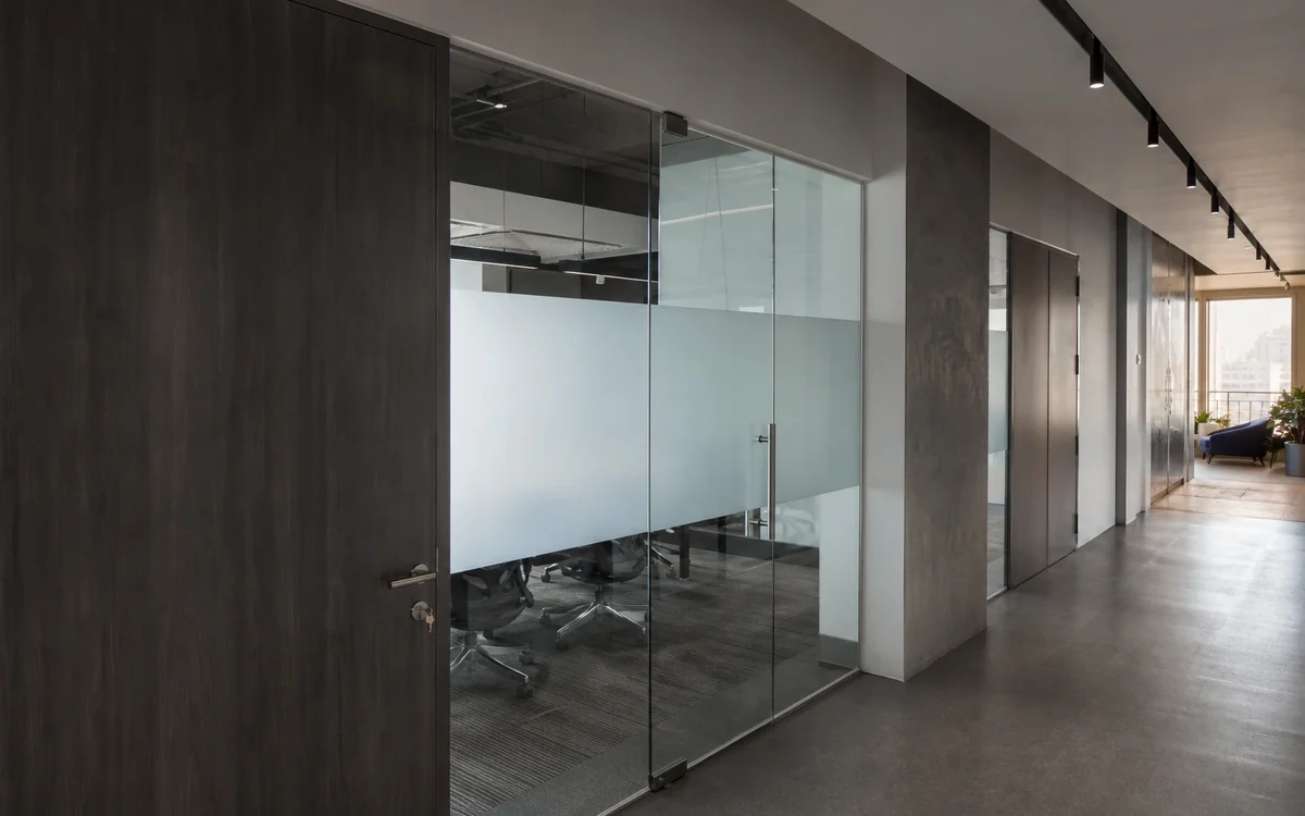 Finished office corridor with a dark timber door, a glass-fronted meeting room with a frosted privacy band and track lighting overhead