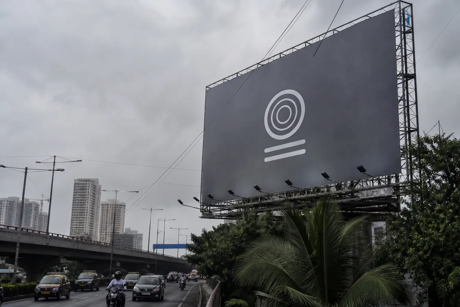 Large blank billboard structure beside a highway with trees and buildings behind